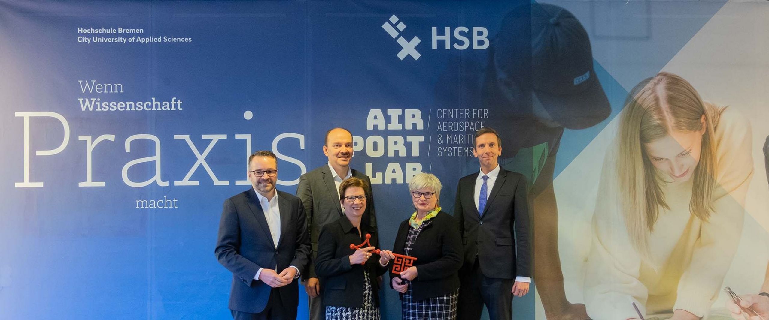 Gruppenfoto, 5 Personen lächeln in die Kamera: Schlüsselübergabe im AIR/PORT/LAB. Personen von links: Staatsrat Tim Cordßen-Ryglewski, Senatorin Dr. Claudia Schilling, Matthias Lehmann, Geschäftsführer der LAT Pilot Academy und Senior Director Pilot Training, Rektorin Prof. Dr. Karin Luckey, Prof. Bastian Gruschka, Dekan der Fakultät 5 – Natur und Technik. 