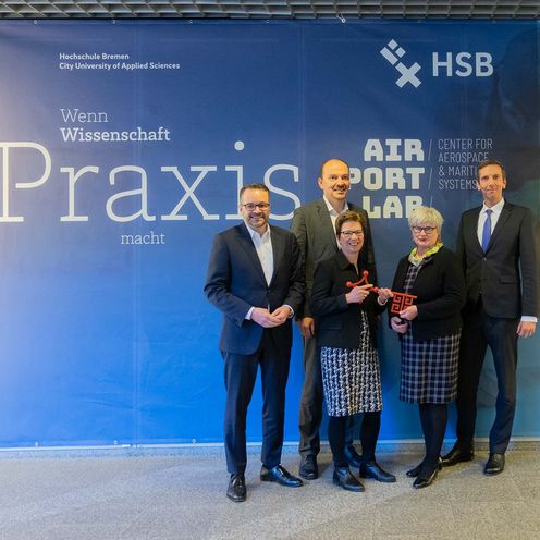 Gruppenfoto, 5 Personen l&auml;cheln in die Kamera: Schl&uuml;ssel&uuml;bergabe im AIR/PORT/LAB. Personen von links: Staatsrat Tim Cord&szlig;en-Ryglewski, Senatorin Dr. Claudia Schilling, Matthias Lehmann, Gesch&auml;ftsf&uuml;hrer der LAT Pilot Academy und Senior Director Pilot Training, Rektorin Prof. Dr. Karin Luckey, Prof. Bastian Gruschka, Dekan der Fakult&auml;t 5 &ndash; Natur und Technik. 