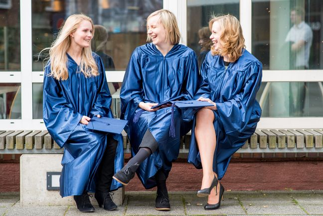 3 Absolventinnen in Talar vor der Mensa