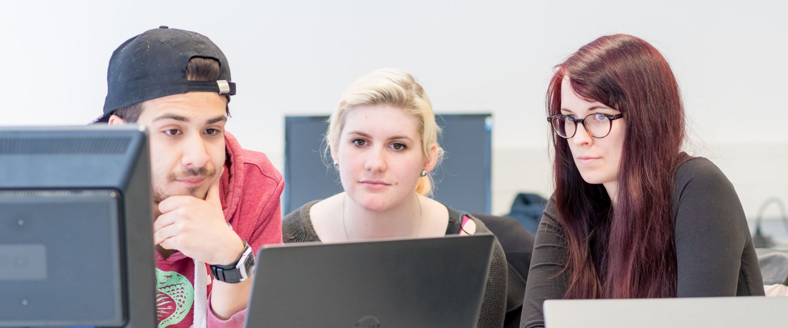 Drei Studierende blicken gemeinsam auf einen Laptop.