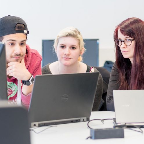 Drei Studierende blicken gemeinsam auf einen Laptop.