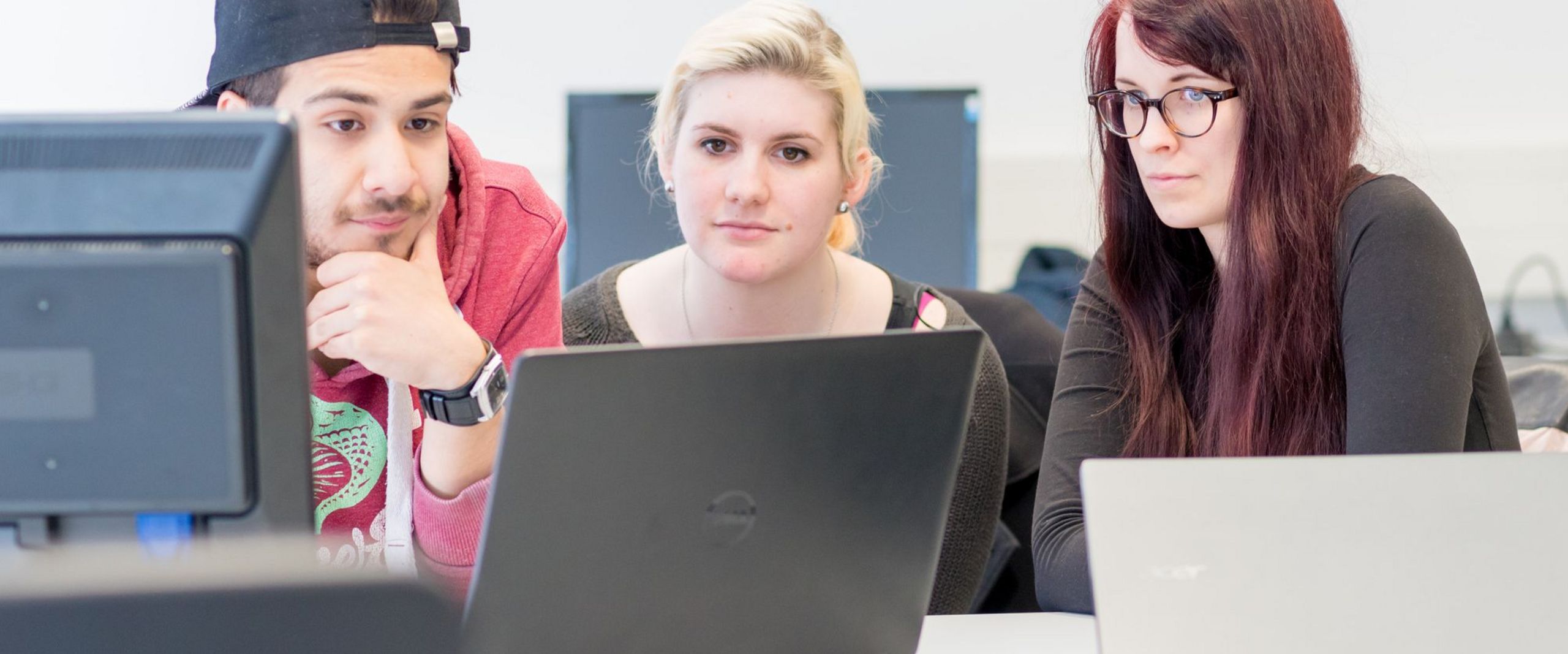 Drei Studierende blicken gemeinsam auf einen Laptop.