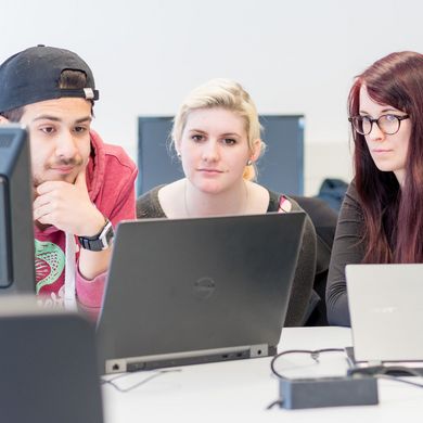 Drei Studierende blicken gemeinsam auf einen Laptop.