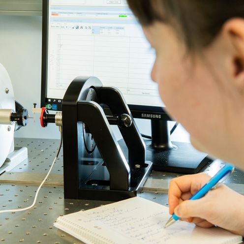 Eine Forscherin beobachtet einen Belastungsversuch mit einem Heuschreckenbein. Im Hintergrund steht ein Computerbildschirm.