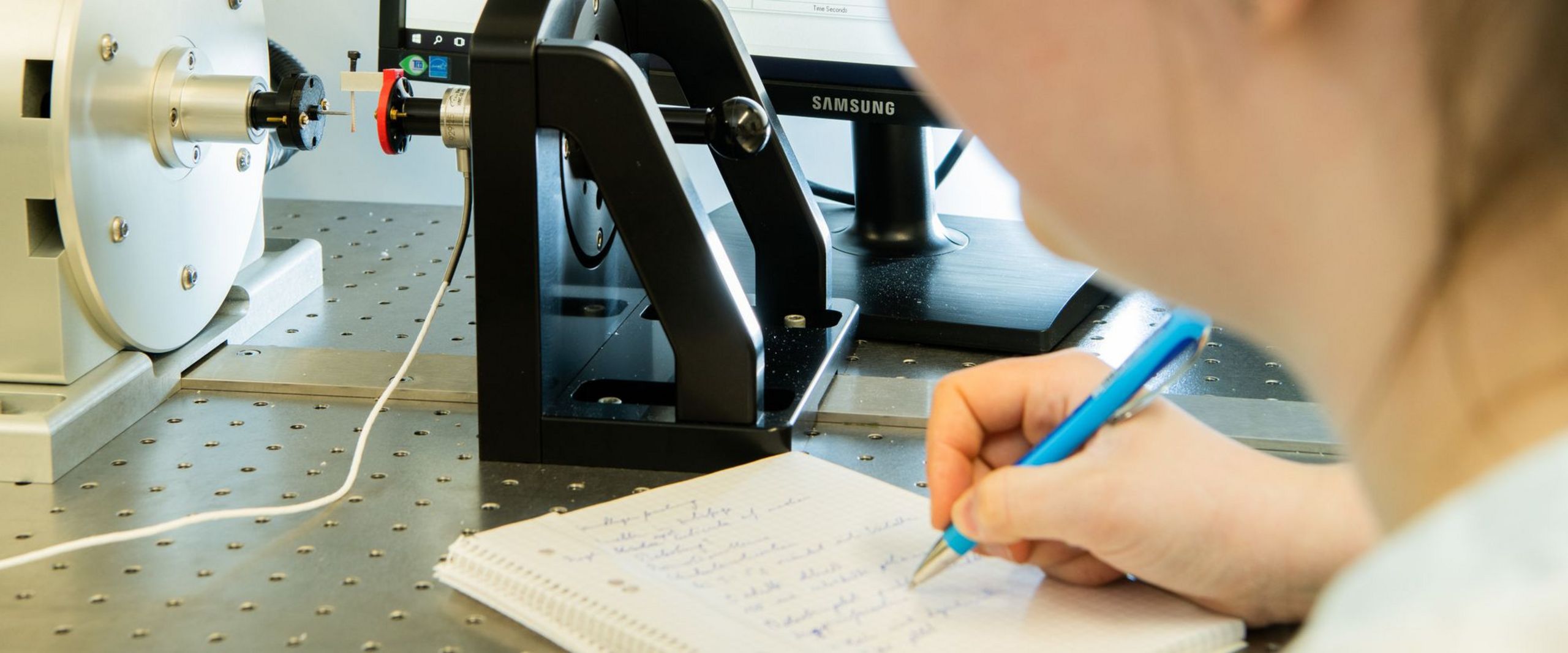 Eine Forscherin beobachtet einen Belastungsversuch mit einem Heuschreckenbein. Im Hintergrund steht ein Computerbildschirm.