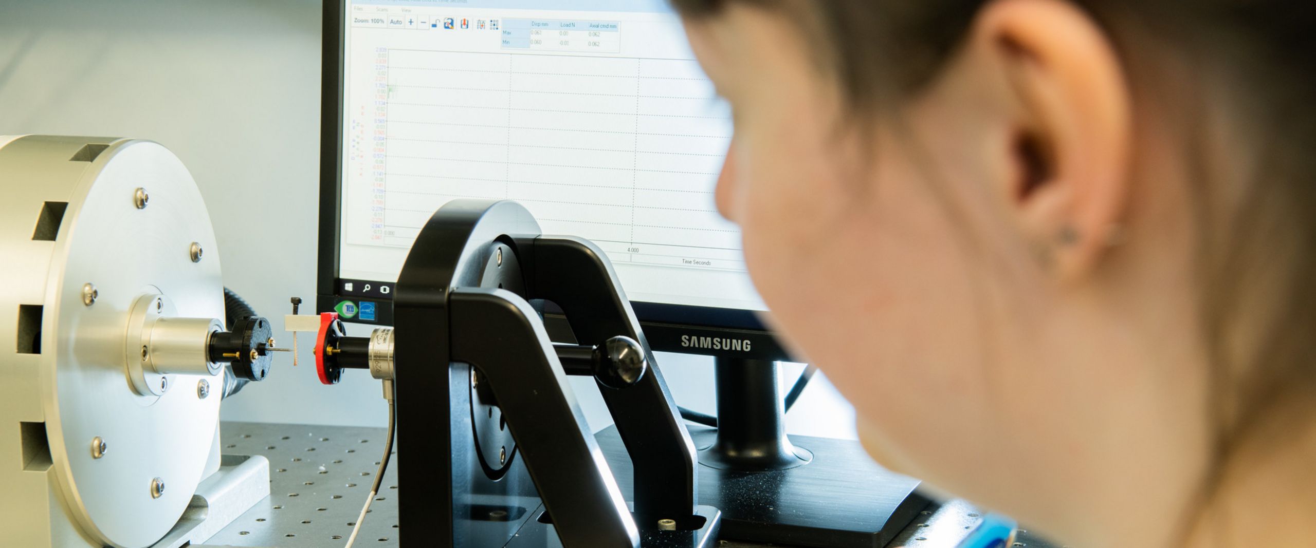 Forschung in der Bionik Eine Forscherin beobachtet einen Belastungsversuch mit einem Heuschreckenbein. Im Hintergrund steht ein Computerbildschirm.