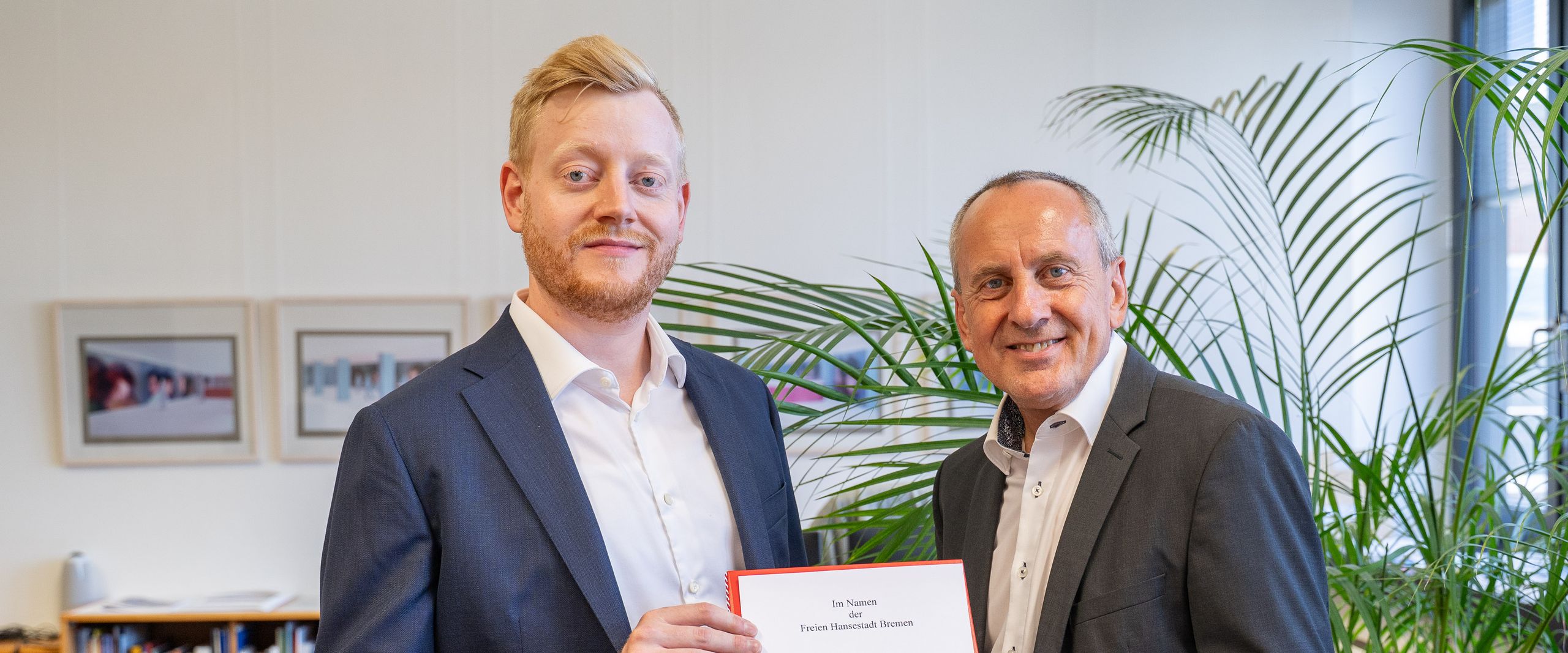 Zwei Männer halten gemeinsam eine Urkunde und schauen in die Kamera