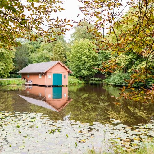 Ein Bootshaus an einem See umgeben von B&auml;umen im Bremer B&uuml;rgerpark.