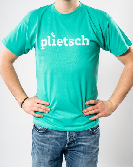 Das Model trägt ein türkises T-Shirt für Herren mit der Aufschrift “plietsch“.