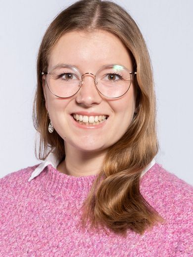 Auf dem Foto ist Louisa Windbrake zu sehen. Sie hat schulterlanges braun-blondes Haar. Sie trägt eine runde Brille und einen pinken Pullover.