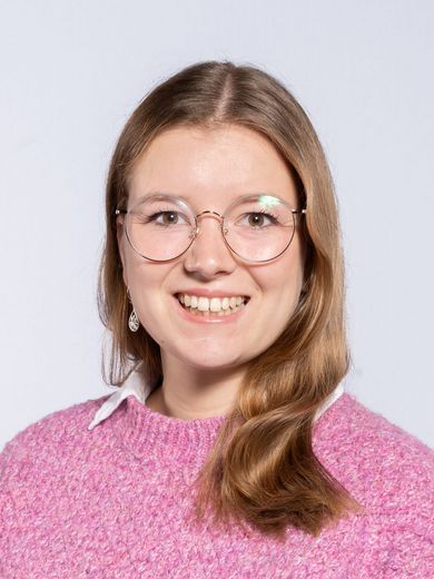 Auf dem Foto ist Louisa Windbrake zu sehen. Sie hat schulterlanges braun-blondes Haar. Sie trägt eine runde Brille und einen pinken Pullover.