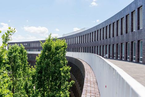 Auf dem Bild ist eine Au&szlig;enansicht des ZIMT-Geb&auml;udes zu sehen. Die Form des Geb&auml;udes &auml;hnelt einem Halbkreis aus dunkelroten Backsteinen. Es sieht sehr modern aus. In der Rundung des Geb&auml;udes wachsen B&auml;ume. 