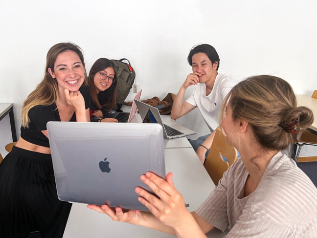 Ein Studierenden-Team des Management Business Game 2022 sitzt zusammen und eine Studentin präsentiert dabei etwas auf ihrem Laptop. Alle Studierenden sind gespannt bei der Sache. 