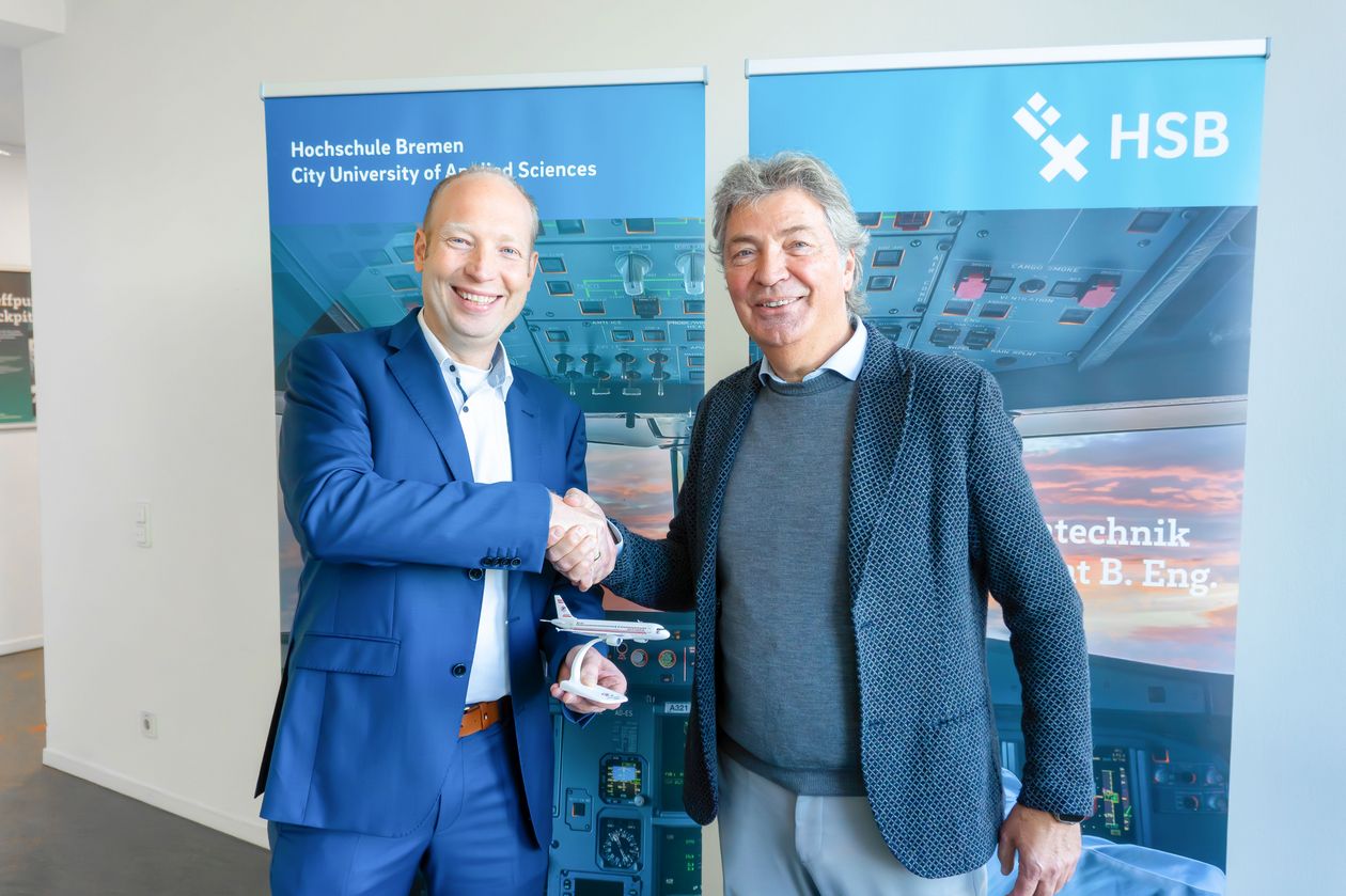 Zwei M&auml;nner sch&uuml;tteln sich die Hand. Der linke h&auml;lt ein kleines Modellflugzeug.