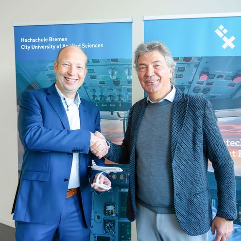 Zwei M&auml;nner sch&uuml;tteln sich die Hand. Der linke h&auml;lt ein kleines Modellflugzeug.