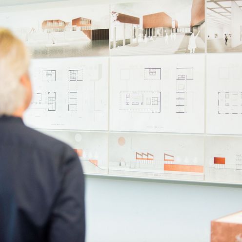 Ein Mann betrachtet architektonische Entw&uuml;rfe an einer Wand.