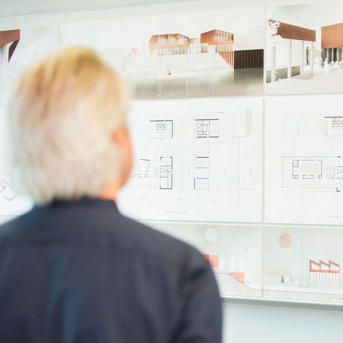 Ein Mann betrachtet architektonische Entw&uuml;rfe an einer Wand.
