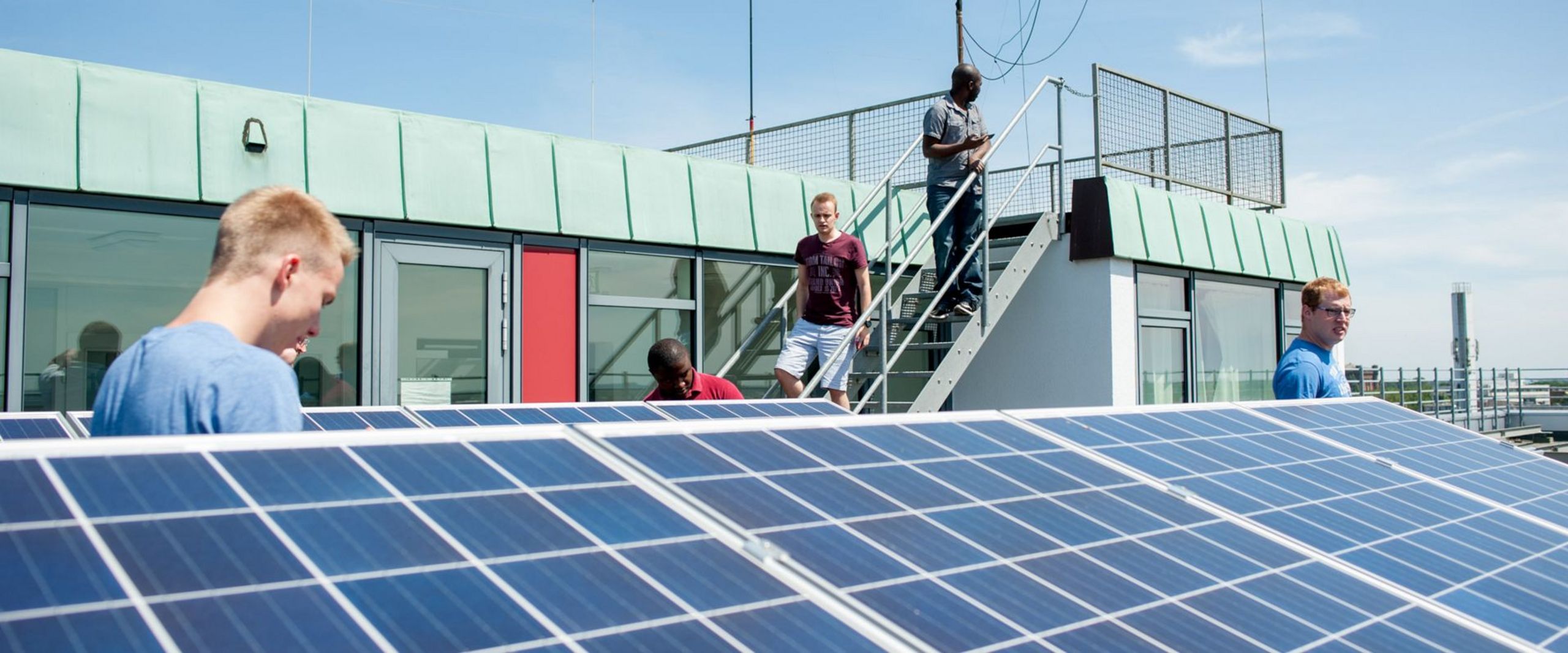Studierende stehen auf dem Dach eines Gebäudes und betrachten eine Solaranlage.
