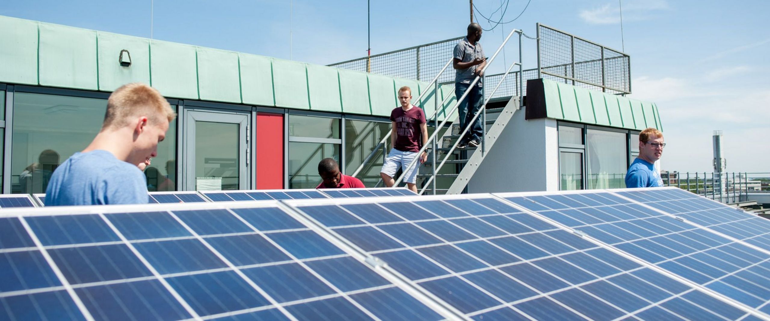 Studierende stehen auf dem Dach eines Gebäudes und betrachten eine Solaranlage.