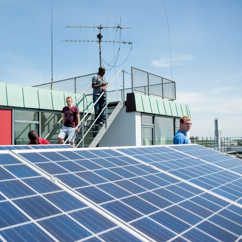 Studierende stehen auf dem Dach eines Geb&auml;udes und betrachten eine Solaranlage.