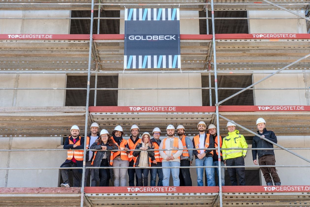 Gruppe von Menschen steht auf einem Baugerüst vor einem Gebäude.