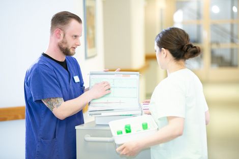 Ein Pfleger und eine Pflegerin besprechen sich an einem Dokumentenwagen auf dem Flur eines Seniorenheimes.