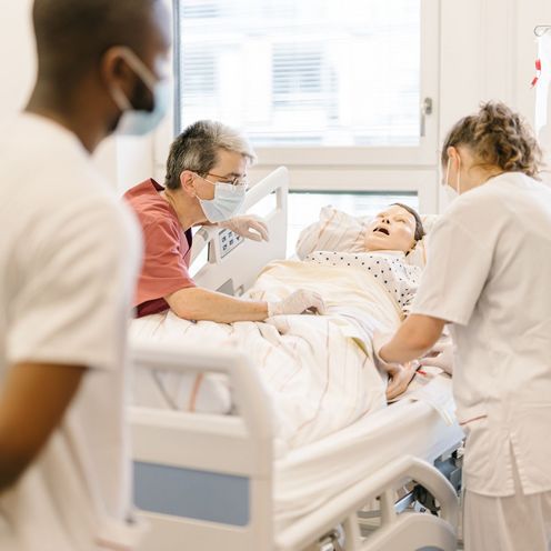 Pflegestudierende &uuml;ben an einem Krankenhausbett mit einer Puppe im Simulationszentrum des Studiengangs.