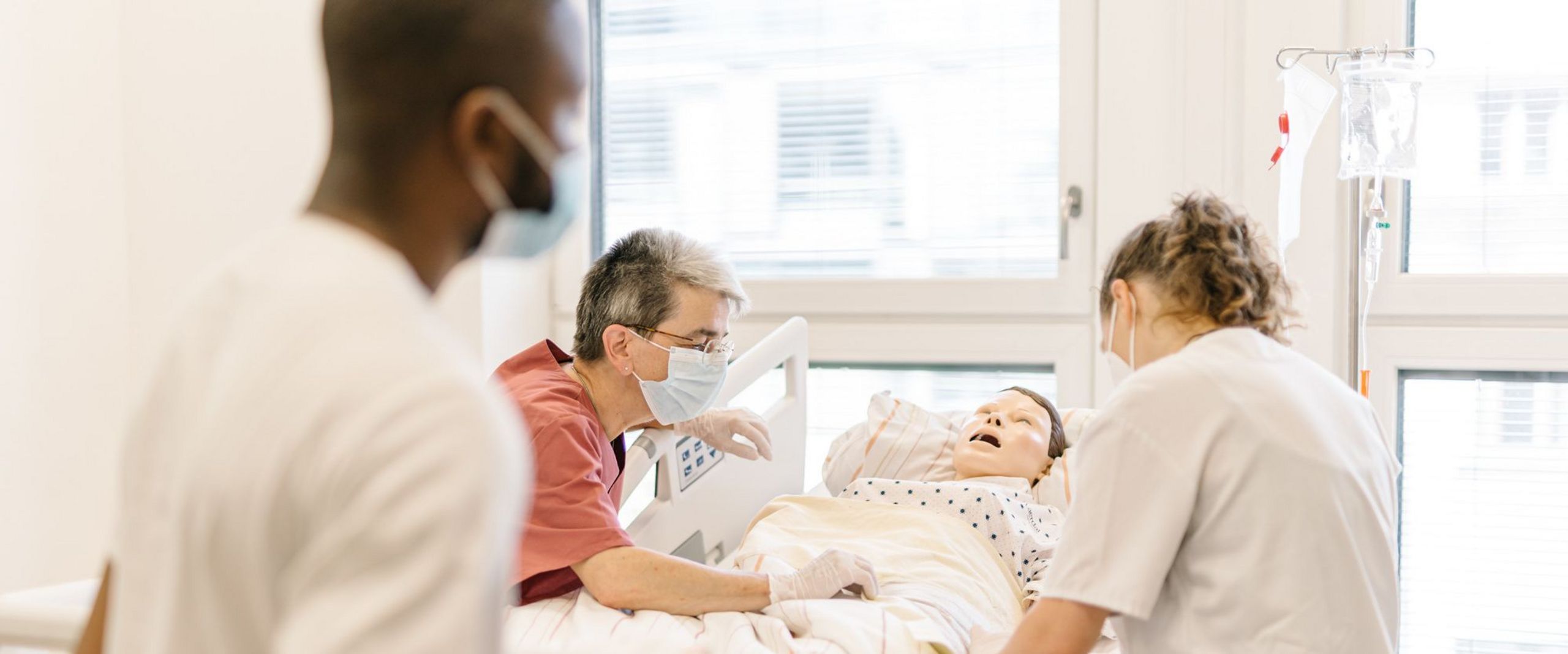 Pflegestudierende üben an einem Krankenhausbett mit einer Puppe im Simulationszentrum des Studiengangs.