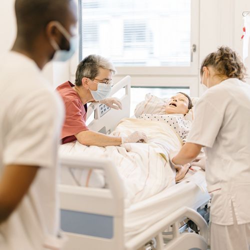 Pflegestudierende &uuml;ben an einem Krankenhausbett mit einer Puppe im Simulationszentrum des Studiengangs.