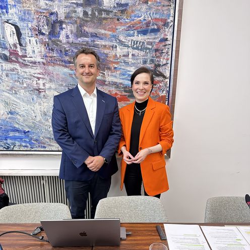 Mann und Frau stehen vor einem gro&szlig;en Gem&auml;lde und lachen in die Kamera