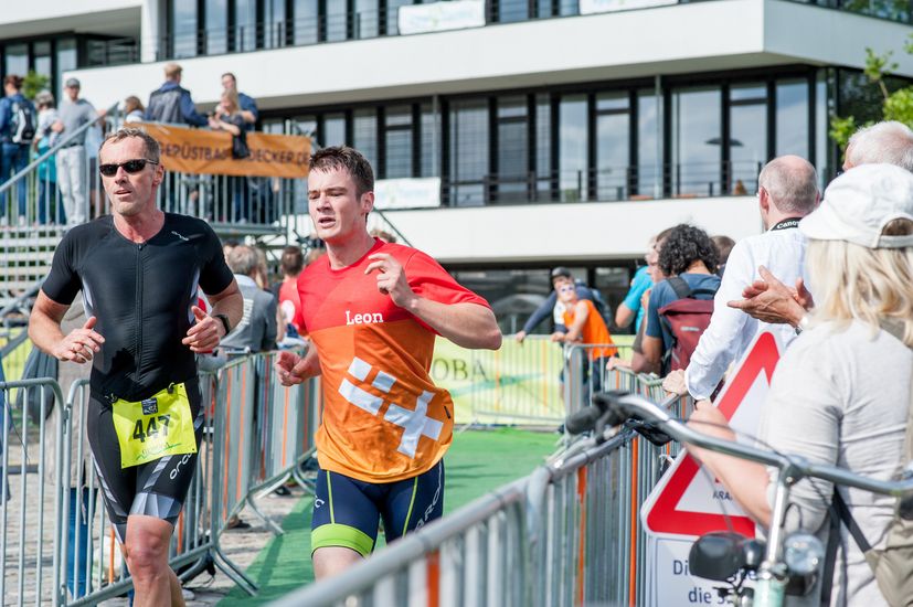 Rennende L&auml;ufer auf der Strecke und an der rechten Seite stehen beobachtende Zuschauer.