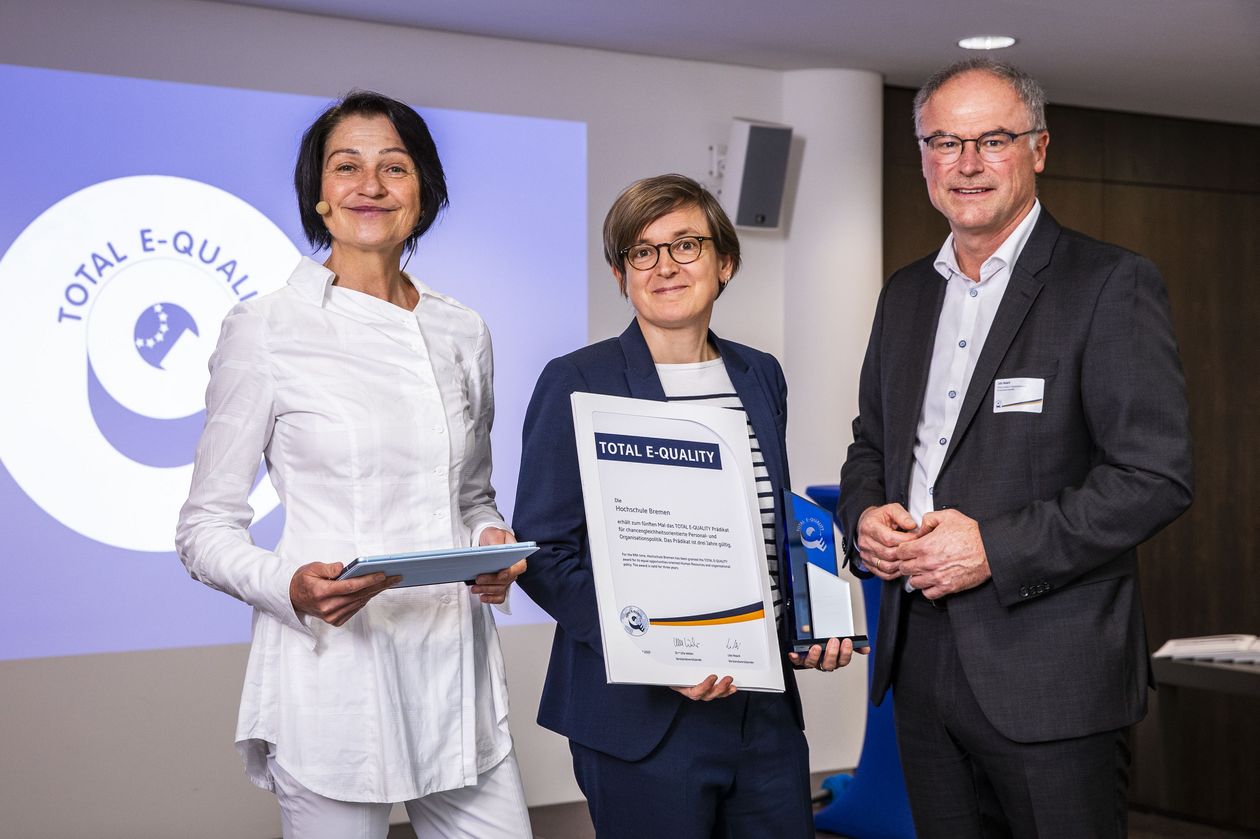 Gruppenbild mit zwei Frauen und einem Mann. Die Frau in der Mitte hält eine Urkunde.