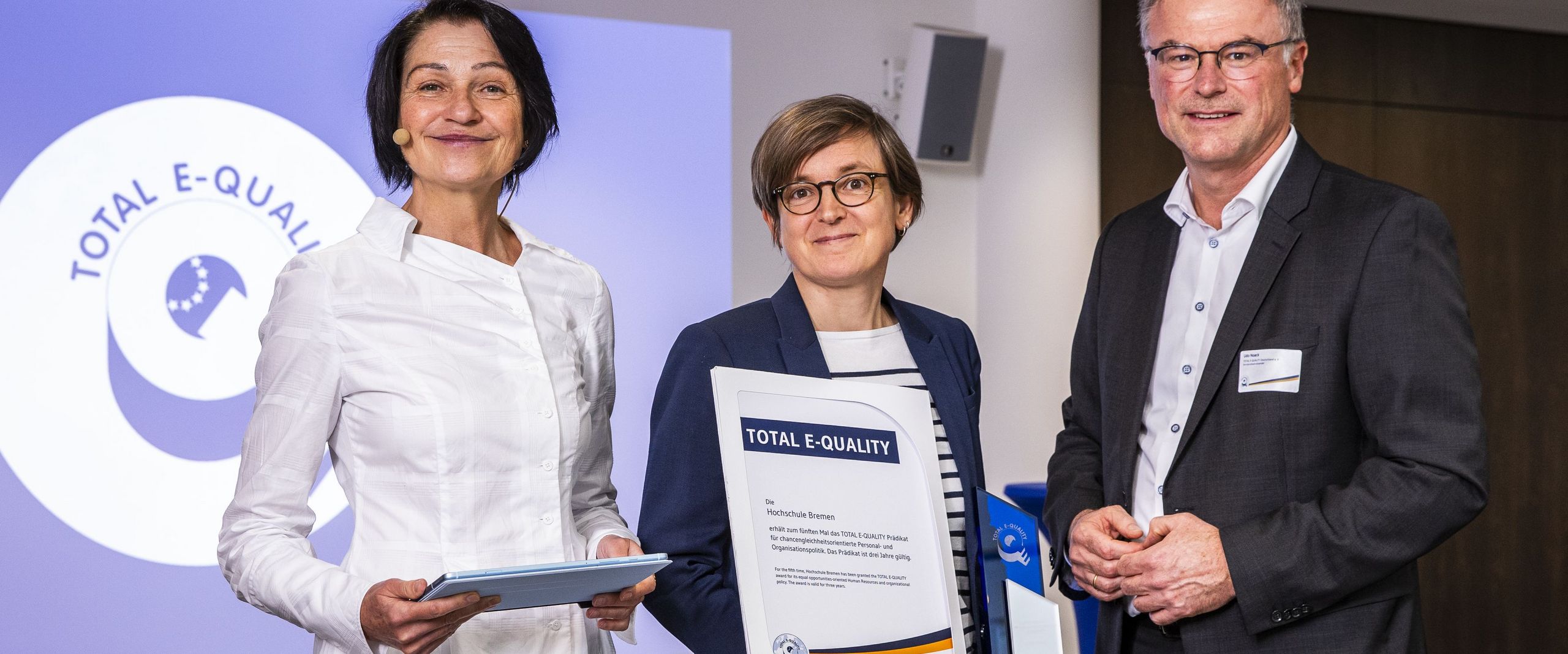 Gruppenbild mit zwei Frauen und einem Mann. Die Frau in der Mitte hält eine Urkunde.