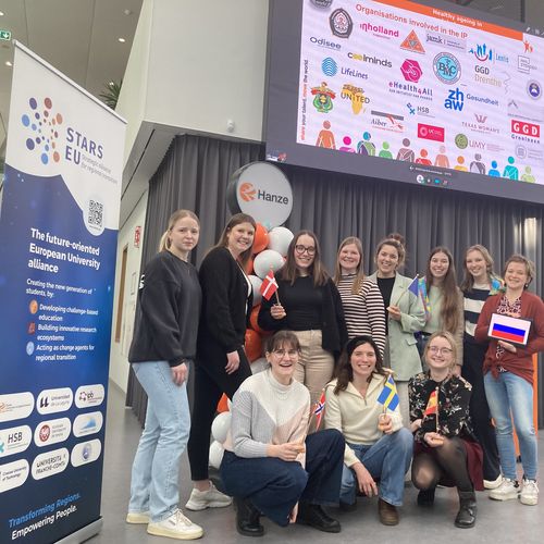 Group with female students. Next to them is a STARS EU roll up. In the background you can see a large monitor with logos. 