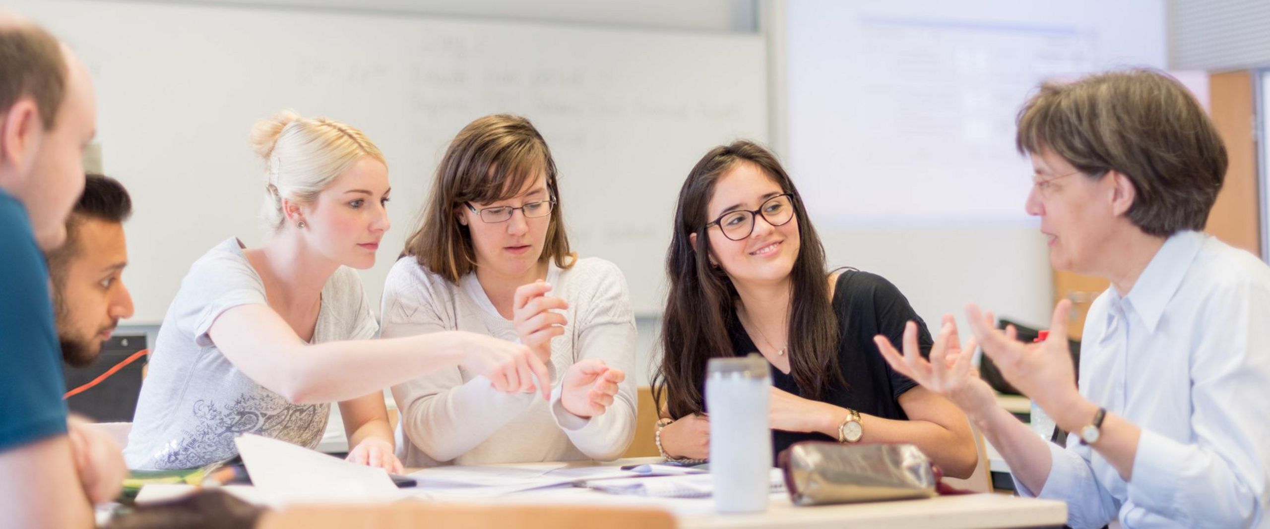 Professorin Martina Röhrich sitzt am Tisch in einem Seminarraum und diskutiert mit einer kleinen Gruppe Studierender.