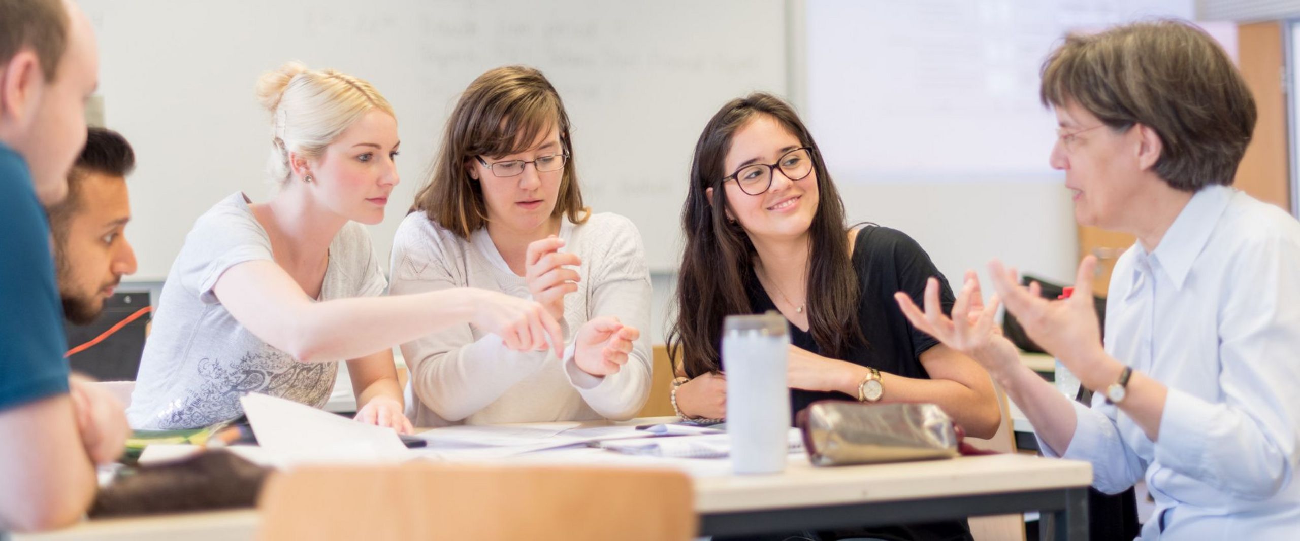 Professorin Martina Röhrich sitzt am Tisch in einem Seminarraum und diskutiert mit einer kleinen Gruppe Studierender.