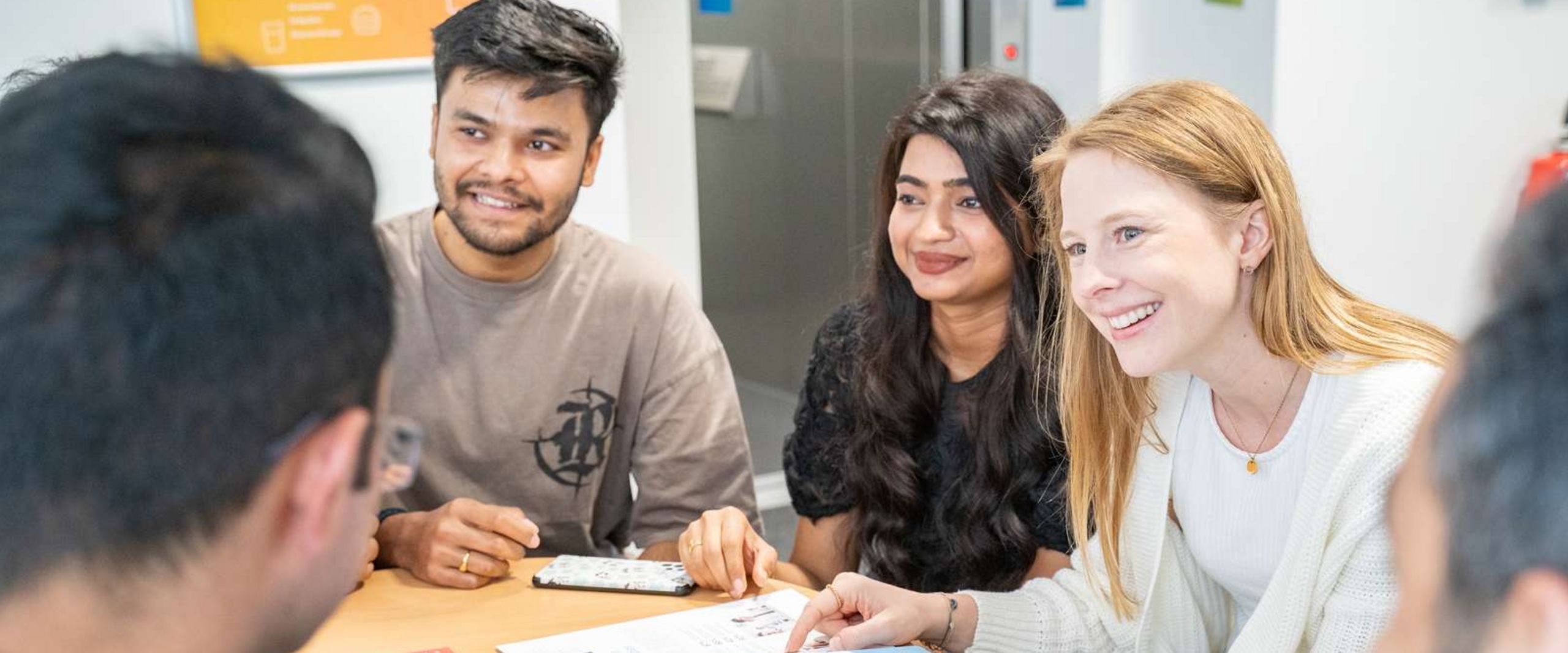 Auf dem Foto ist eine Gruppe von Studierenden zusehen. Sie sitzen um einen runden Tisch und unterhalten sich. 