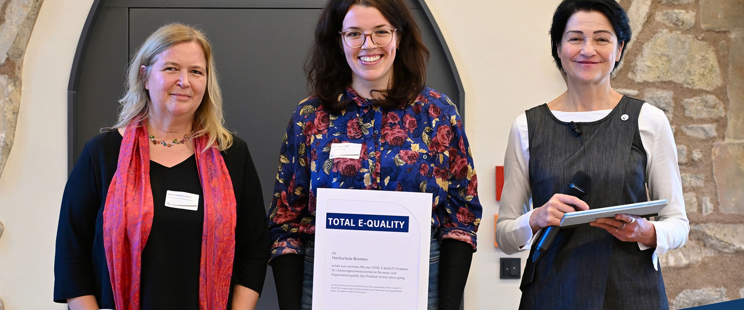 Drei Frauen stehen nebenenander. Luise Kilian in der Mitte h&auml;lt die Urkunde des TOTAL E-QUALITY Pr&auml;dikats in der Hand. Alle l&auml;cheln. 