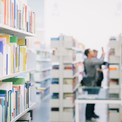 Studierende zwischen Bücherregalen in der Bibliothek.