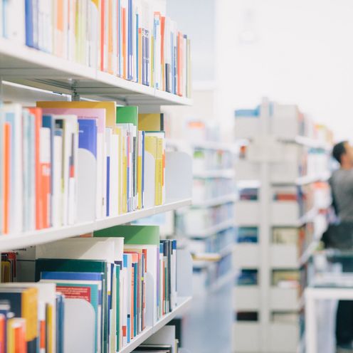 Studierende zwischen B&uuml;cherregalen in der Bibliothek.