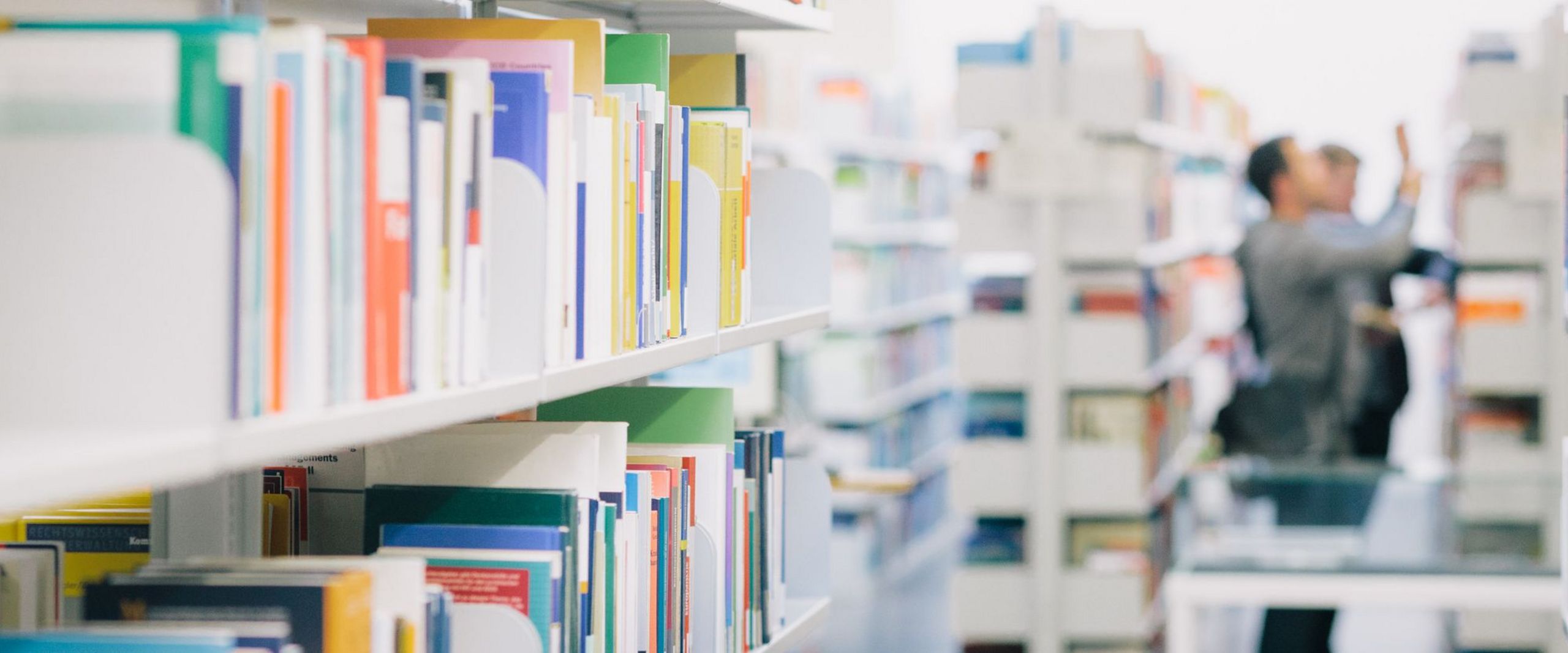 Studierende zwischen Bücherregalen in der Bibliothek.