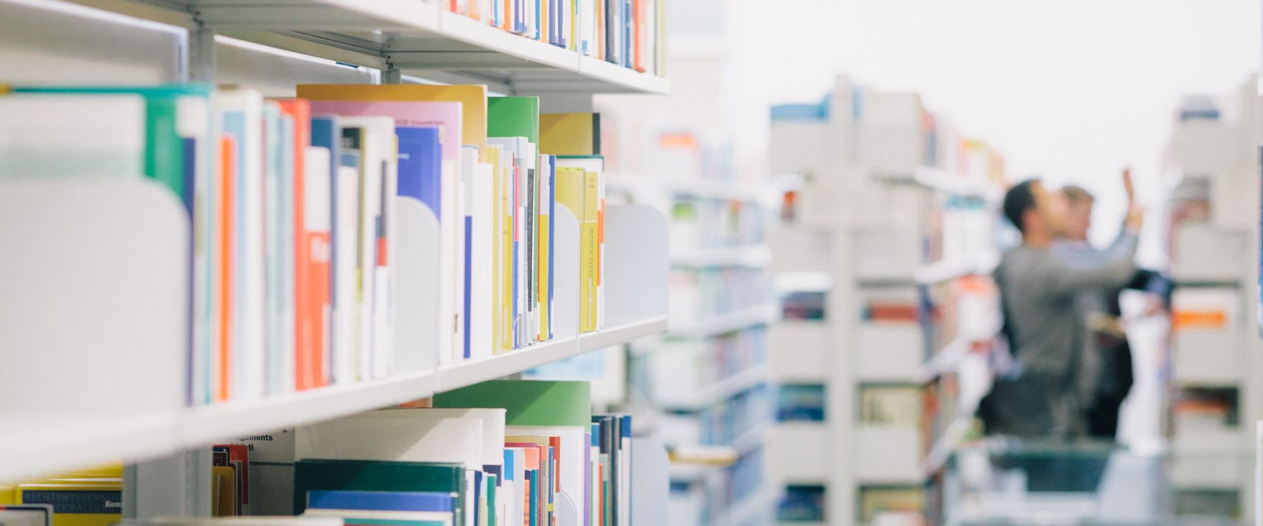 Studierende zwischen Bücherregalen in der Bibliothek.