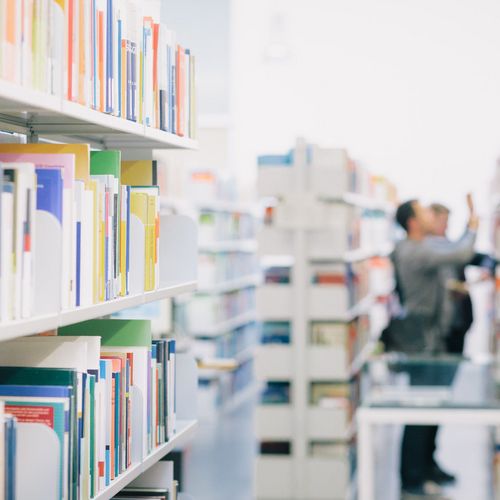 Studierende zwischen B&uuml;cherregalen in der Bibliothek.