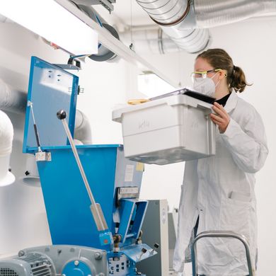 Eine Studierende auf einer Leiter hält einen Behälter an den Trichter einer Maschine. 