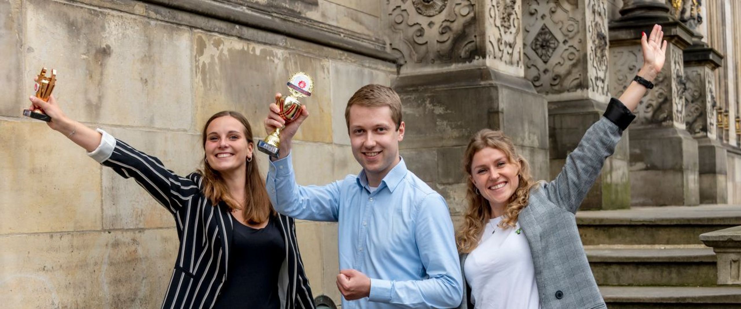3 junge Gründer:innen jubelnd mit Pokal vor Schütting