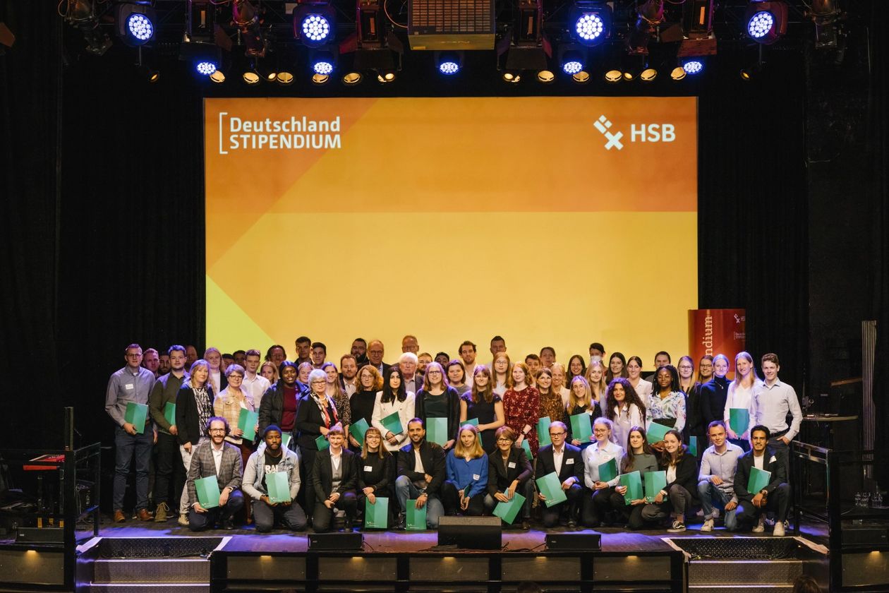 Gruppenfoto Deutschlandstipendiat:innen 2022 Gruppenbild mit lachenden Männern und Frauen auf einer Bühne