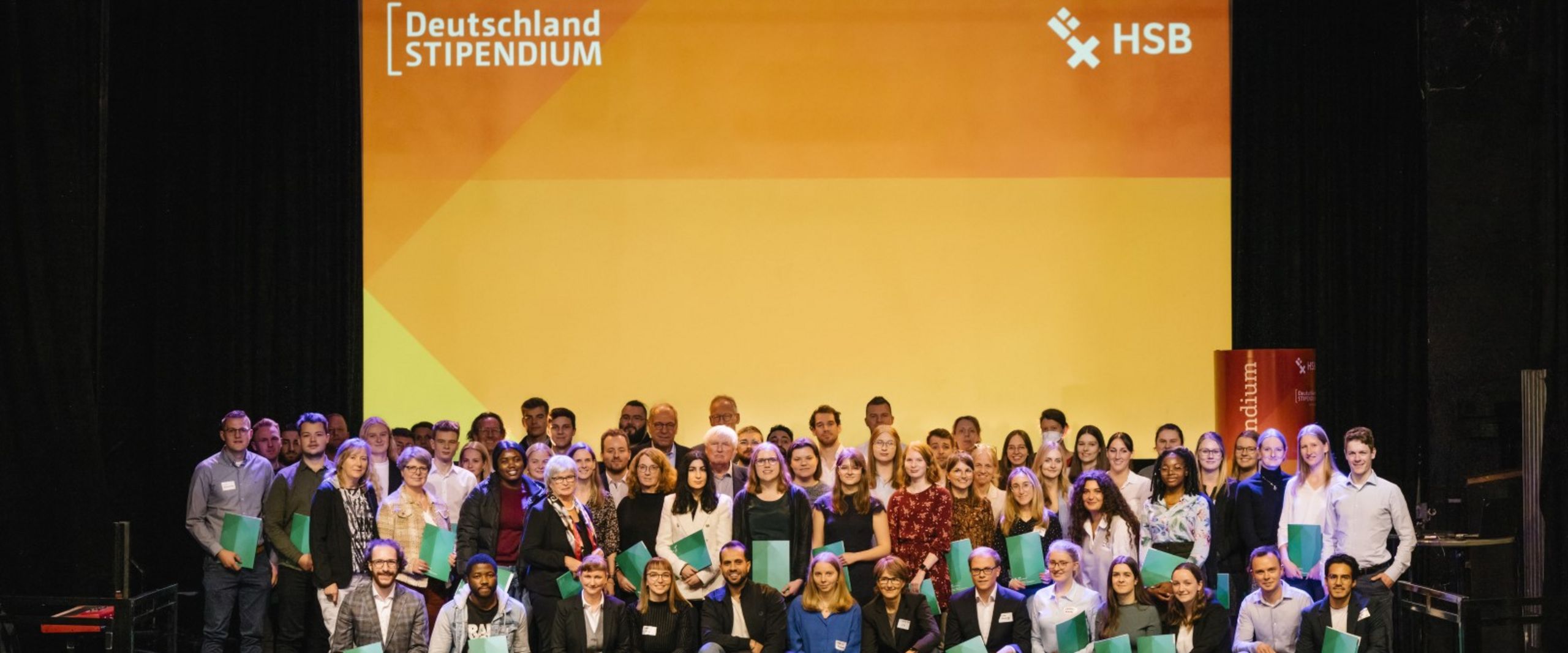 Gruppenfoto Deutschlandstipendiat:innen 2022 Gruppenbild mit lachenden Männern und Frauen auf einer Bühne