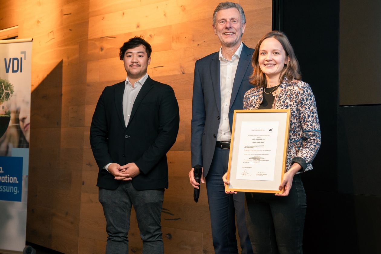 gruppenbild mit zwei Männern und einer Frau. Die Frau hält eine Urkunde.