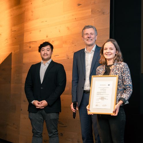 gruppenbild mit zwei M&auml;nnern und einer Frau. Die Frau h&auml;lt eine Urkunde.
