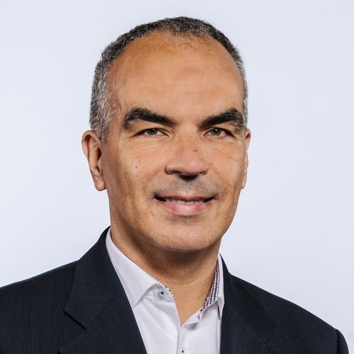 Auf dem Bild ist Martin Holi zu sehen. Er hat kurzes Haar und trägt ein weißes Hemd unter einem dunkel Jacket. 